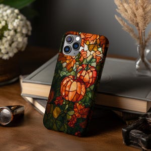 Puede incluir: Una funda para tel&eacute;fono con un dise&ntilde;o de vitral con calabazas y hojas de oto&ntilde;o. La funda es negra y tiene un recorte para el objetivo de la c&aacute;mara.