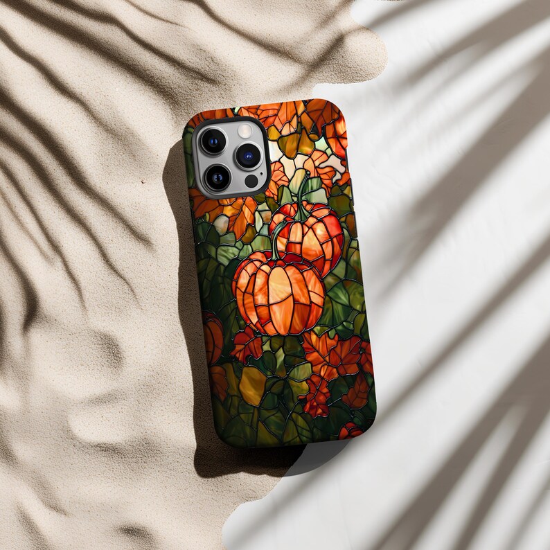 Puede incluir: Una funda para tel&eacute;fono de estilo vitral con un dise&ntilde;o de calabazas y hojas en tonos naranja, verde y marr&oacute;n.