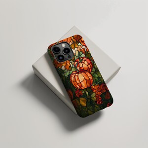 Puede incluir: Una funda para tel&eacute;fono con un dise&ntilde;o de vitral con calabazas naranjas y hojas verdes. La funda es negra y tiene un recorte para la c&aacute;mara del tel&eacute;fono.