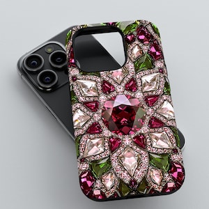 May include: A decorative phone case featuring a jewel-encrusted design. The case has a central large, dark pink gem surrounded by smaller pink, clear, and green gems. The case is resting on a black phone.