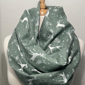 May include: A green infinity scarf with a white deer and pine tree pattern.