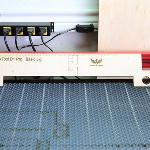 Puede incluir: Un jig de madera para una cortadora l&aacute;ser xTool D1 Pro. El jig est&aacute; etiquetado como "xTool D1 Pro Basic Jig" y tiene un logotipo de "Brighton Art Works".