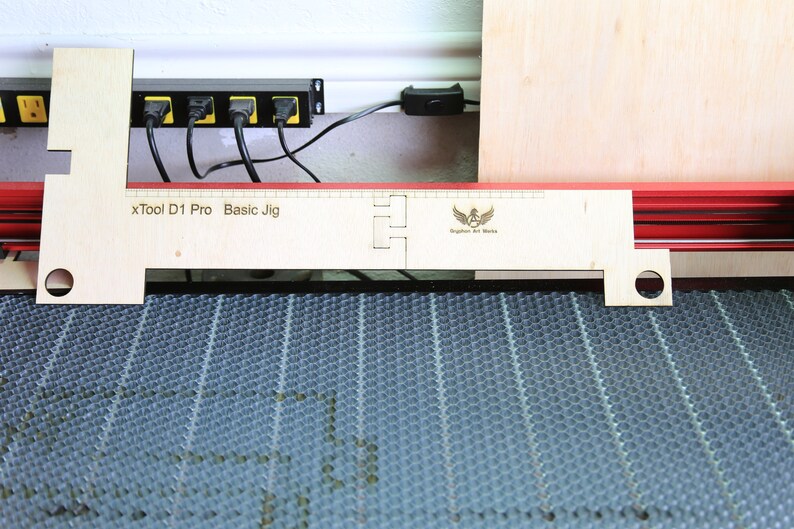 Puede incluir: Un jig de madera para una cortadora l&aacute;ser xTool D1 Pro. El jig est&aacute; etiquetado como "xTool D1 Pro Basic Jig" y tiene un logotipo de "Brighton Art Works".