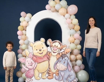 Puede incluir: Un gran arco blanco decorado con globos pastel, con recortes de Winnie the Pooh, Piglet, Tigger y Eeyore. Un niño pequeño y una mujer adulta están cerca.