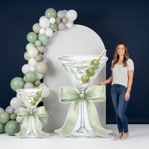 Op de afbeelding: Grote martini glazen uitsparingen met groene olijven en ijs, versierd met een groene strik. Een ballonnenboog in groen- en wittinten vult het thema aan. Perfect voor een feest of evenement.