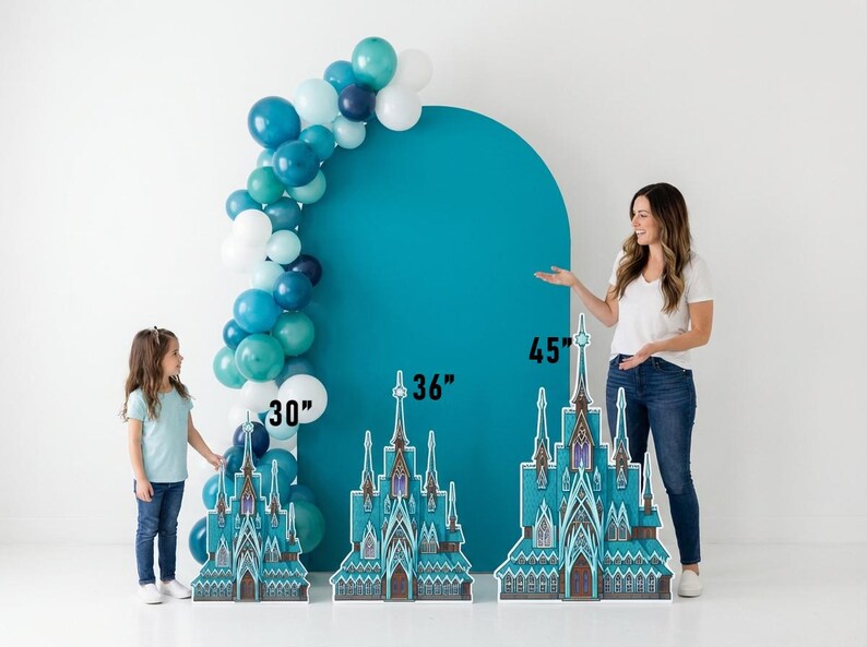 May include: A teal backdrop with a balloon arch and three castle cutouts. The castle cutouts are 30, 36, and 45 inches tall. The balloon arch features white, teal, and navy blue balloons. A woman and a child are standing near the cutouts.