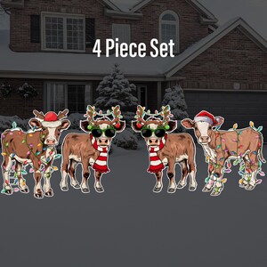 May include: A set of four Christmas-themed cow yard decorations. Each cow is wearing a Santa hat and has colorful lights strung around it. The set includes the text "4 Piece Set".