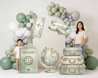 Pode incluir: Uma exibição com tema de viagem com um passaporte, um cartão de embarque, um avião, um globo e malas empilhadas. A cena é decorada com balões verdes, cinzentos e brancos. Uma mulher e uma criança estão perto dos adereços.