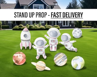 Op de afbeelding: Een set stand-up rekwisieten met een raket, astronauten en planeten. De rekwisieten zijn geschilderd in aquarel stijl met roze, wit, grijs en blauwe kleuren. De rekwisieten zijn perfect voor een ruimte-thema feest of evenement.