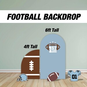 May include: Two football-themed backdrops for photo booths. The backdrop on the left is 4 feet tall and features a brown football with white stitching. The backdrop on the right is 6 feet tall and features a light blue background with a white football and the text "1st Year Down".