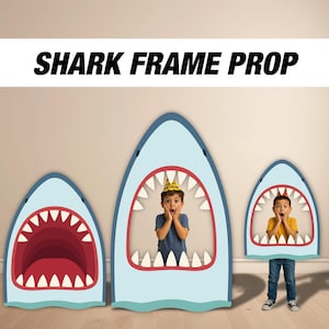 May include: Three shark-shaped photo props with open mouths, in varying sizes. The props are light blue with red and white details. The text "SHARK FRAME PROP" is displayed above the props. Two children are inside the props.