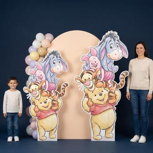 May include: Two large, freestanding cutouts of Winnie the Pooh and friends, including Tigger, Piglet, and Eeyore, are displayed. A young boy and a woman stand nearby. A balloon arch and a peach-coloured backdrop complete the scene, set against a dark blue background.