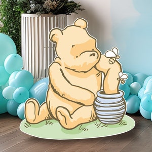Puede incluir: Un oso de dibujos animados amarillo sentado en un parche de hierba verde, sosteniendo un tarro de miel a rayas azul y blanco. Dos abejas amarillas vuelan alrededor del oso.