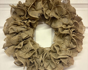 May include: A rustic burlap wreath with a ruffled design. The wreath is circular, with a natural brown color, and is made of woven burlap fabric. The wreath is suitable for indoor or outdoor use and is a decorative item for the home.