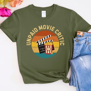 May include: A green t-shirt featuring a retro-style graphic that reads "Unpaid Movie Critic" with a film clapboard and popcorn bucket.
