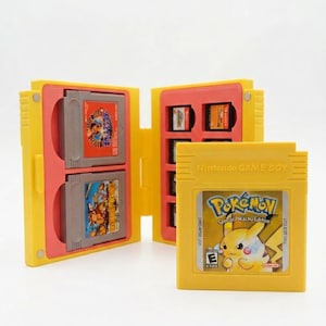 Op de afbeelding: Een gele plastic opbergdoos voor handheld gamecartridges met een scharnierend ontwerp en rode binnenvakken. De doos bevat verschillende grijze gamecartridges, terwijl een gele Nintendo Game Boy-cartridge voor Pokemon Special Pikachu Edition ervoor staat.