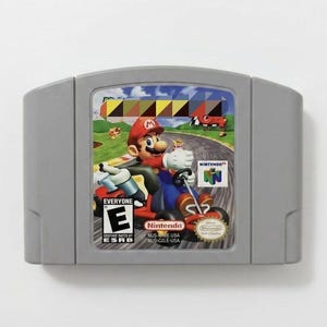 May include: A gray Nintendo 64 video game cartridge featuring a label with Mario driving a red go-kart on a race track. The label includes the Nintendo 64 logo, an ESRB Everyone E rating symbol, and the text Nintendo NUS-NME-USA NUS-GME-USA.
