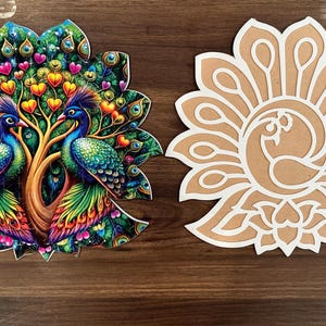 Op de afbeelding: Twee decoratieve stukken met een pauwthema. De ene is een kleurrijke, gedetailleerde illustratie van twee pauwen met een boom van harten. De andere is een lasergesneden ontwerp van een pauw in een bloemvorm, met een lichtbruine achtergrond en witte contouren.