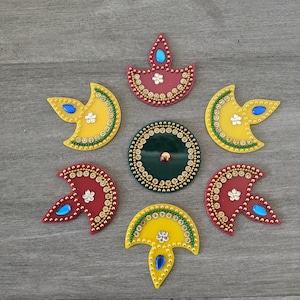 May include: A set of seven decorative diya stickers in yellow, red, and green with gold accents. The stickers feature a traditional diya design with a small flame and a beaded border.
