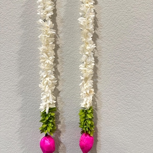 May include: Two vertical garlands with white flower petals, green leaves, and pink bulbous ends hang against a gray wall. The garlands are suspended from white hooks at the top.
