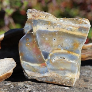 Puede incluir: Una losa pulida de piedra ágata con capas translúcidas en tonos gris, blanco y ámbar. La superficie muestra bandas naturales, pequeñas inclusiones circulares y una textura suave y reflectante con fracturas visibles en toda la cara.