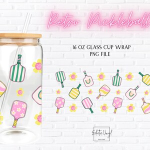 May include: A clear 473 ml glass cup with a bamboo lid and straw, decorated with a pickleball design. The design includes pickleball paddles and flowers in pink, yellow, and green. The text "Retro Pickleball" is displayed in pink neon.