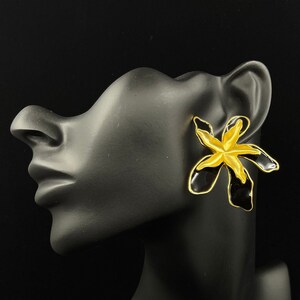 May include: A pair of black and gold flower-shaped earrings. The earrings are made of metal and have a black enamel finish with gold accents.