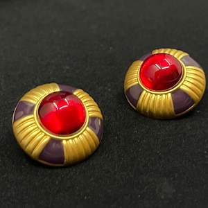 May include: A pair of gold tone earrings with a purple enamel base and a red glass cabochon in the center.