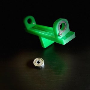 May include: A green plastic tool with a ruler and two metal ball bearings. One ball bearing is attached to the tool and the other is separate.