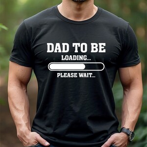 May include: Black t-shirt featuring the white text "DAD TO BE LOADING... PLEASE WAIT..." and a loading bar graphic. The t-shirt is a crew neck style.