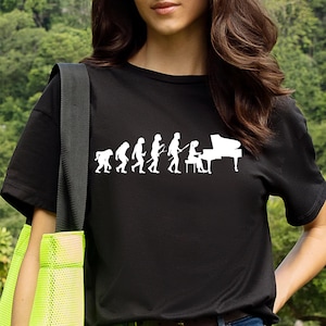 May include: Black t-shirt featuring a white graphic of the evolution of a pianist. The design shows the progression from ape to human playing a grand piano. A fun and unique design for music lovers.