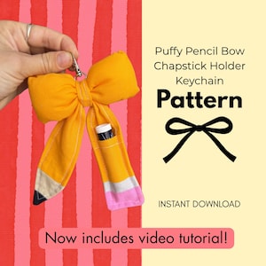Puede incluir: Un llavero de tela amarillo con forma de lápiz y cierre metálico. El lazo presenta una punta negra, una banda gris y un extremo rosa. El texto dice: Puffy Pencil Bow Chapstick Holder Keychain Pattern, Instant Download, Now includes video tutorial!