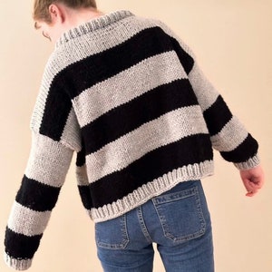 May include: A black and grey striped sweater with a relaxed fit. The sweater is made of a soft, chunky yarn and has a slightly cropped length.