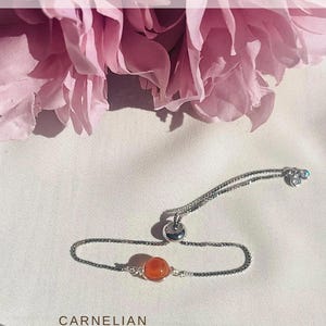 Op de afbeelding: Een zilveren armband met een carneoolsteen. De armband heeft een fijne ketting en een schuifsluiting. De tekst "SILVER BRACELET" en "CHOOSE FROM ANY CRYSTAL IN OUR COLLECTION" staan bovenaan. Het woord "CARNELIAN" staat onderaan.