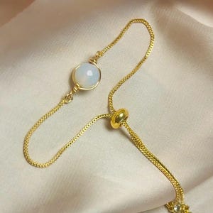 May include: A gold-toned adjustable ring featuring a vibrant orange OPALITE stone. The ring has a delicate chain design with a small, sparkling accent stone.