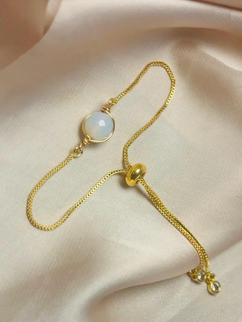 May include: A gold-toned adjustable ring featuring a vibrant orange OPALITE stone. The ring has a delicate chain design with a small, sparkling accent stone.
