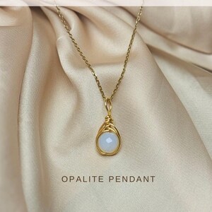 Op de afbeelding: Een goudkleurige ketting met een opaliethanger. De hanger heeft een lichtblauwe-witte kleur, draadgewikkeld in goud. De afbeelding bevat de tekst "OPALITE PENDANT" en "PENDANT MADE TO FIT ANY GOLD CHAIN". De ketting is niet inbegrepen.
