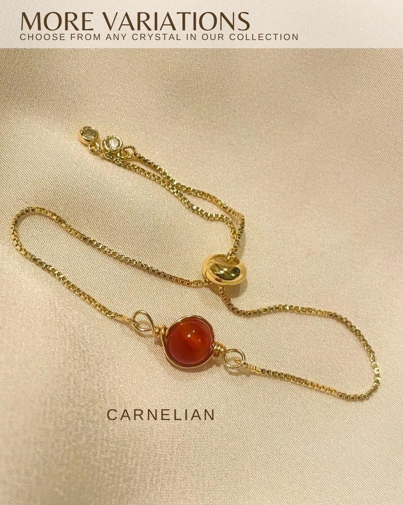 Op de afbeelding: Een goudkleurige verstelbare ring met een heldere oranje carneoolsteen. De ring heeft een delicaat kettingontwerp met een kleine, sprankelende accentsteen. De tekst "MORE VARIATIONS" en "CARNELIAN" zijn zichtbaar.