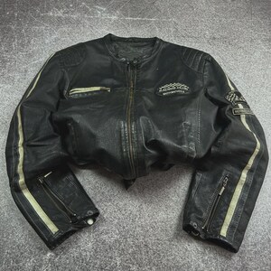 Puede incluir: Chaqueta de moto de cuero negro con cremallera, dos bolsillos delanteros y rayas blancas en las mangas. La chaqueta tiene un parche de Racing Club Motorcycle y un parche de bandera a cuadros.