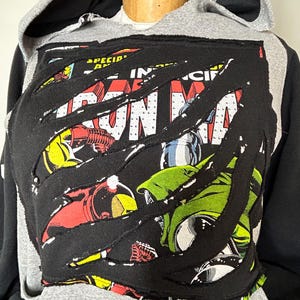 May include: A gray and black hoodie with a ripped comic book design featuring Iron Man and the text "Iron Man" on the front.