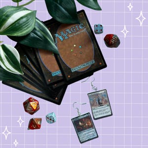 以下が含まれることがあります： ミニチュアのMagic: The Gatheringカードを使用したイヤリングのペア。赤、オレンジ、青の多面体ゲーム用ダイスがいくつか添えられ、茶色と青の裏面を持つMagic: The Gatheringカードの束と一緒に配置されています。