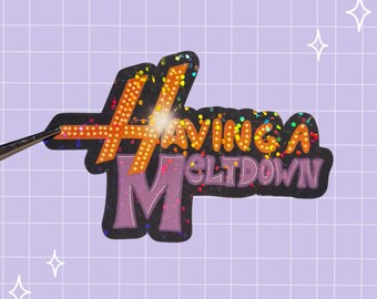 May include: A die-cut sticker featuring the text Having A Meltdown in a bold, stylized font. The letters are orange with a dotted pattern and a holographic glitter finish, set against a black background with a purple outline.