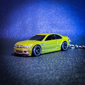 May include: A yellow toy car model of a BMW M3, with black wheels and a detailed interior. The car is on a blue background.