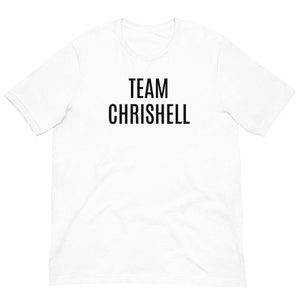 May include: White t-shirt with the text "TEAM CHRISHELL" printed in black. The shirt has short sleeves and a crew neck. The text is centered on the front of the shirt.