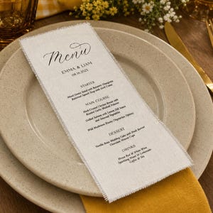 Puede incluir: Una tarjeta de menú rectangular de color blanco roto con bordes deshilachados y texto impreso en negro que dice Menu, Emma & Liam, 08.16.2023, seguido de secciones para Starter, Main Course, Dessert y Drinks, sobre un plato beige moteado.