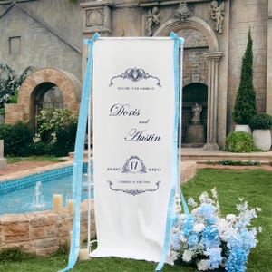 May include: A tall white rectangular wedding welcome sign on a metal stand, featuring dark blue text reading Welcome to the wedding of Doris and Austin, August 17 Sunday, Cathedral of Saint Paul, decorated with light blue ribbons on the sides.