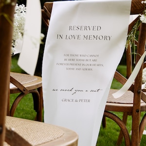 May include: A white fabric sign draped over a wooden cross-back chair with a woven seat. The sign features black text reading: RESERVED IN LOVE MEMORY, FOR THOSE WHO CANNOT BE HERE TODAY BUT ARE FOREVER PRESENT IN OUR HEARTS, TODAY AND ALWAYS, we saved you a seat, GRACE & PETER.