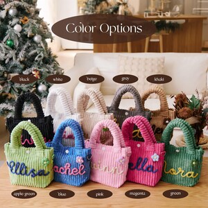 May include: A collection of corduroy tote bags in various colors, including black, white, and pink. Each bag features a handle and a name embroidered on the front. The color options are displayed above the bags.
