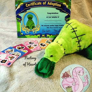 Puede incluir: Un pato de peluche verde con costuras cosidas y un certificado de adopción. El certificado dice "Felicitaciones por la adopción de... Damos la bienvenida a otro Webkin feliz a su hogar para siempre." El certificado está firmado por "Blue Fole" y "Ms. B". El juguete está sobre una superficie peluda marrón claro con varias pegatinas de colores.