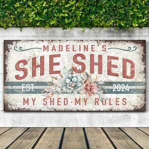 May include: A rustic metal sign with the text "Madeline's She Shed Est. 2024 My Shed My Rules" in red, white, and blue lettering. The sign is decorated with a floral design and has a distressed look.